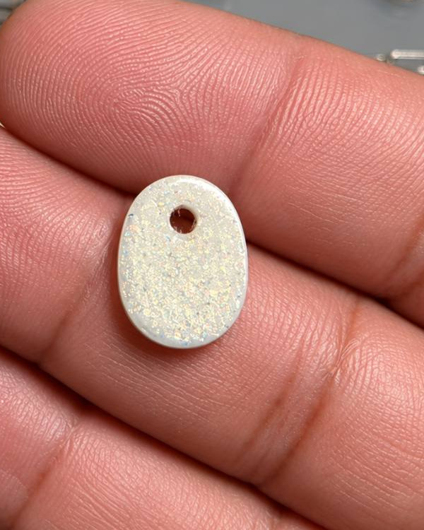 Oval ivory-colored resin pendant with a small hanging hole and subtle shimmer, resting on fingers