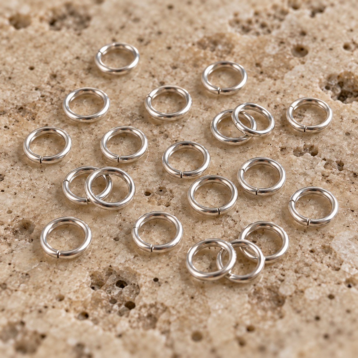 Close view of sterling silver jump rings representing 22g wire on travertine.