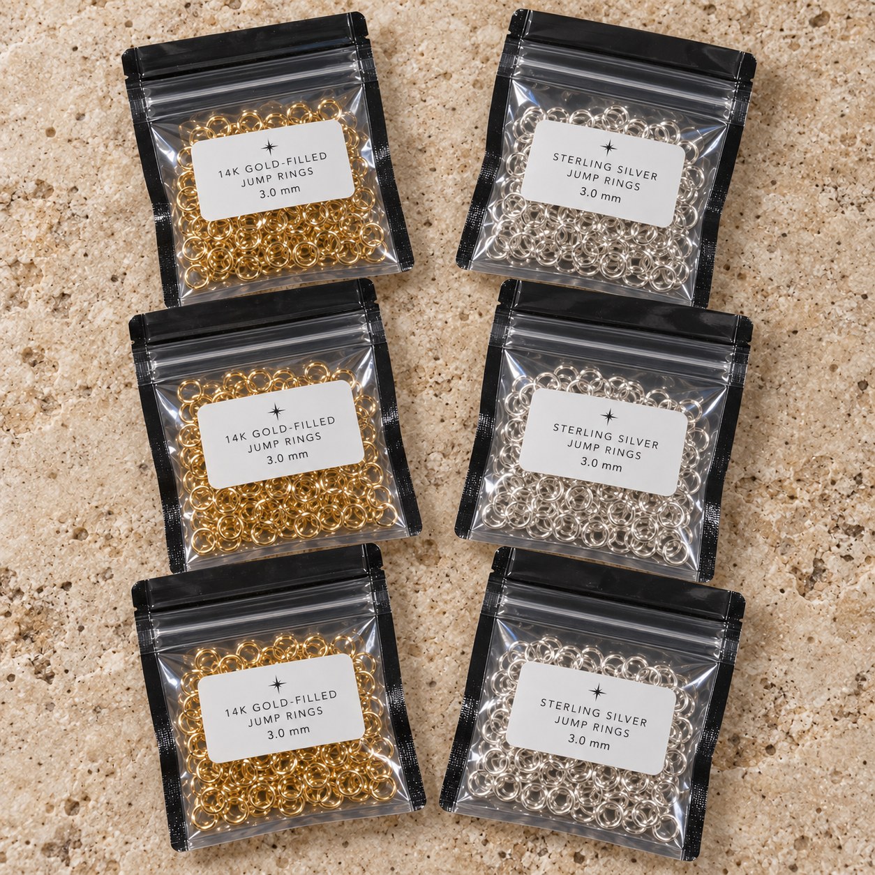 Six labeled bags of sterling silver and 14K gold-filled jump rings on travertine.