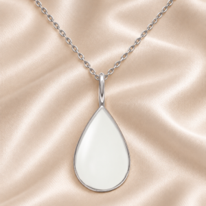 Illustrated teardrop Mother's Milk pendant design with a silver-colored setting and chain on ivory satin.