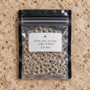 One resealable bag of sterling silver jump rings on a travertine countertop.